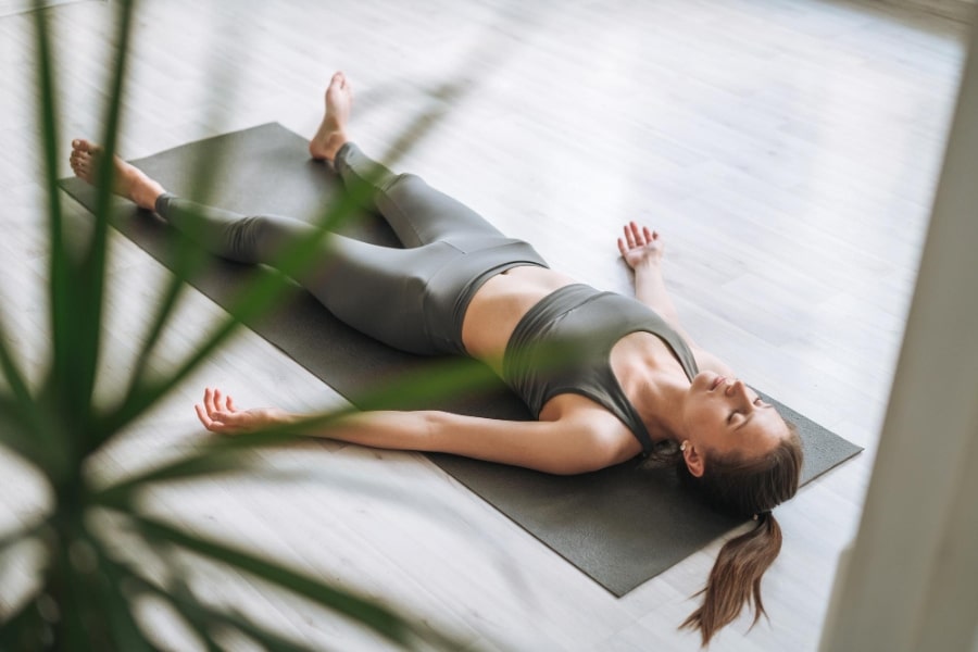 Žena ležící na podložce v relaxační poloze savasana, ilustrace meditace yoga nidra